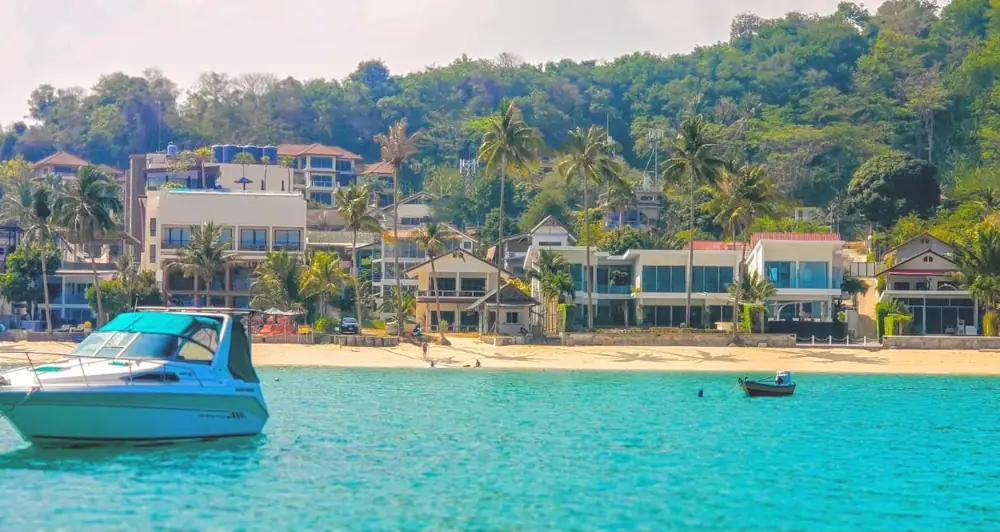Ao Yon Beach seen from the water: turquoise sea, golden sand and beach houses below green hills